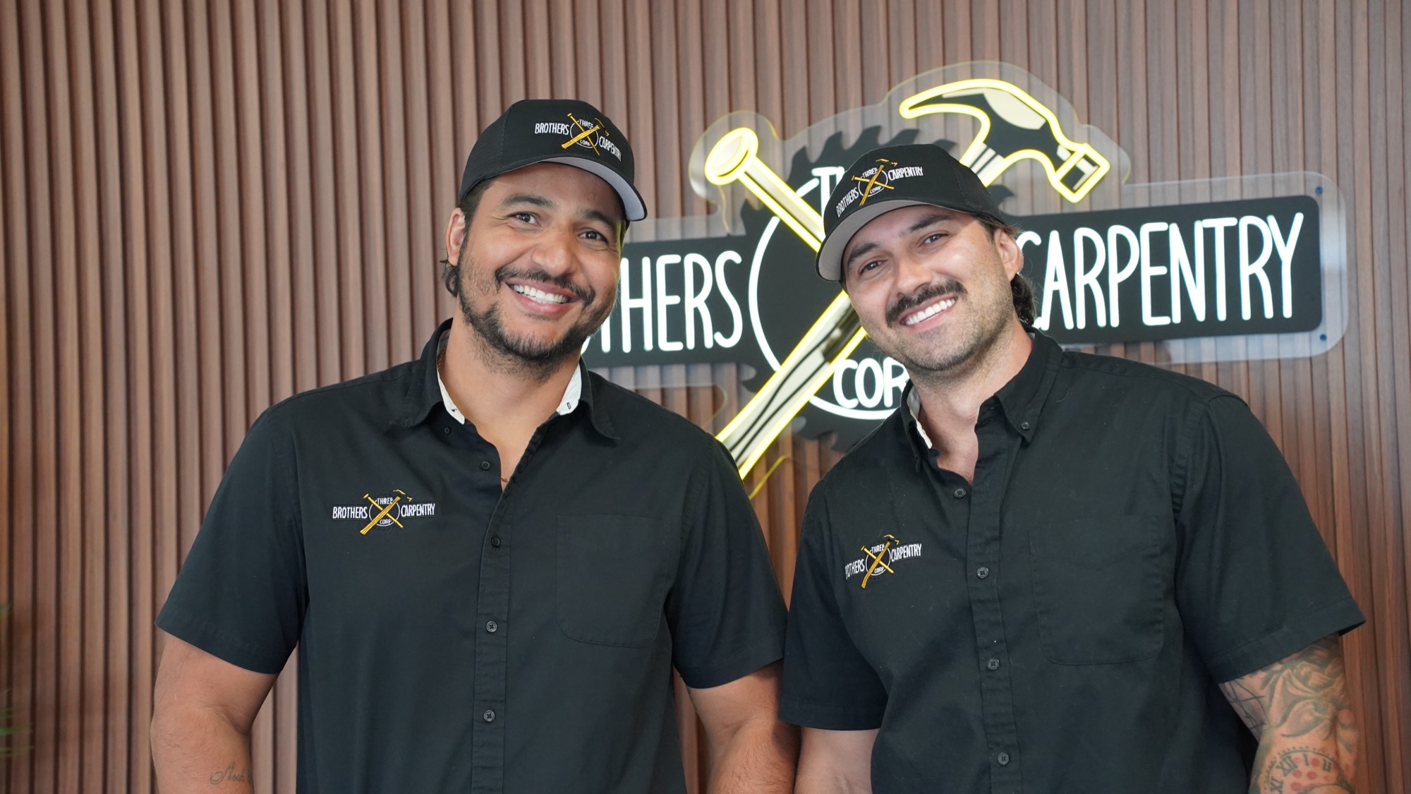Diego Santiago and Cristiano Marques in front of the Three Brothers Carpentry sign